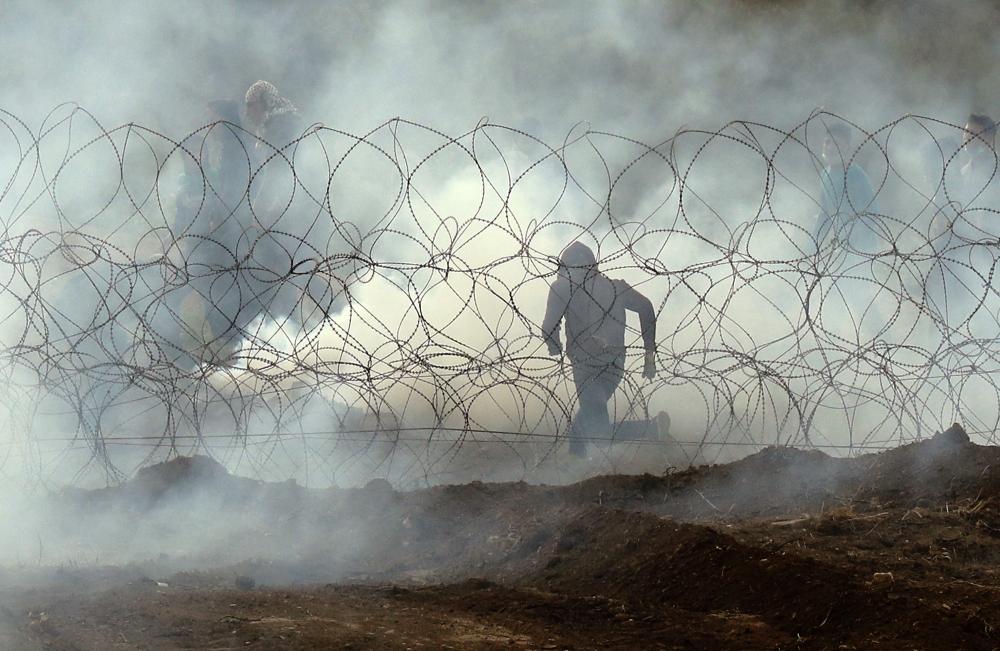 TOPSHOT - This picture taken on March 30, 2019 from the southern Israeli kibbutz of Nahal Oz across the border from the Gaza Strip, shows a Palestinian protester running away from the border fence, as Palestinians demonstrate to mark the first anniversary of the 